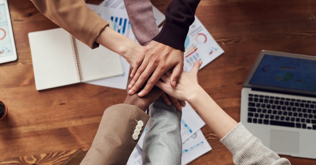 Diverse professionals unite for teamwork around a wooden table with laptops and documents.