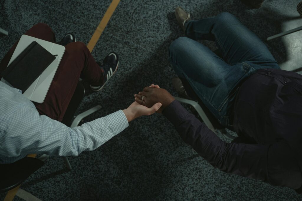 Two individuals share a supportive handshake during a counseling session indoors.